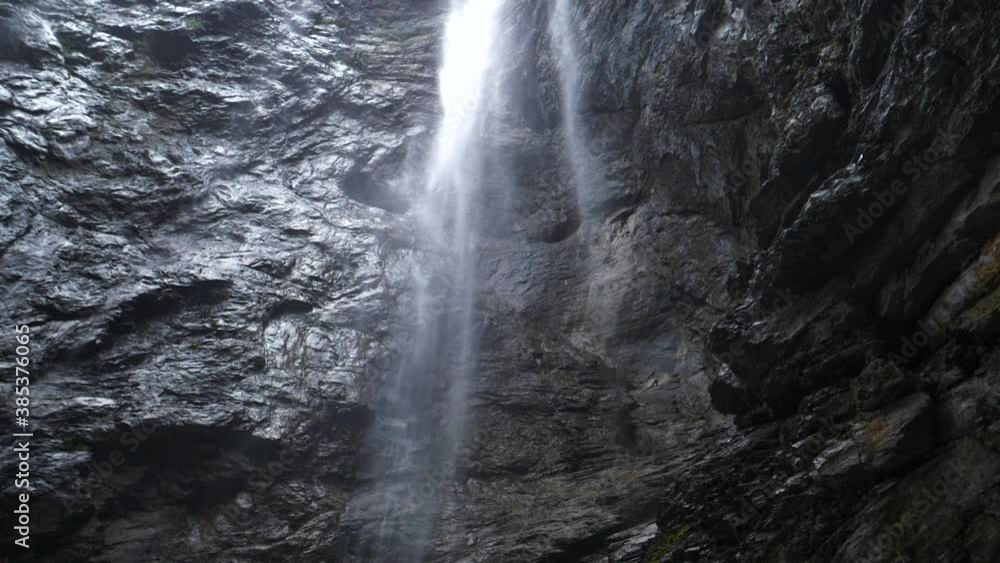 following slow motion of a waterfall inside massive glacier canyon, rain drops falling through frame with wet stones background following slow motion of a waterfall inside massive glacier canyon, rain drops falling through frame with wet stones background