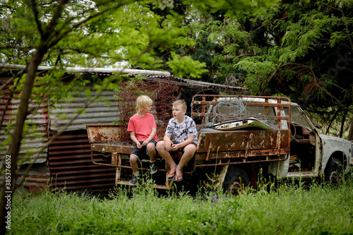 Two boys sitting on ruins of old truck on abandoned farm. Urban exploration, run down property