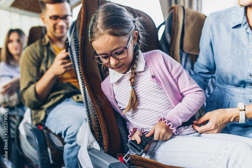 Cute girl putting on seat belt and traveling in bus with mother.