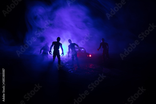 photo of a car stopped on the road lighting up a zombies. Silhouette terrible zombie night near the car. Miniature decoration.