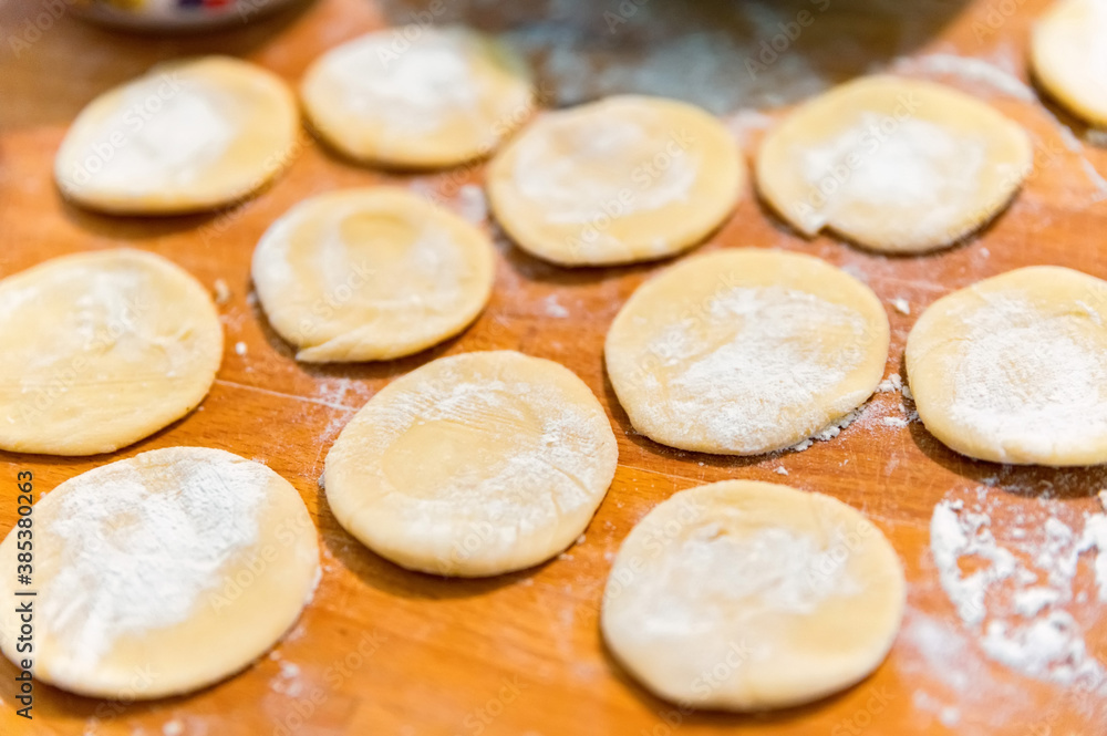 Close-up of small crumpets from raw dough covered with flour on wooden board