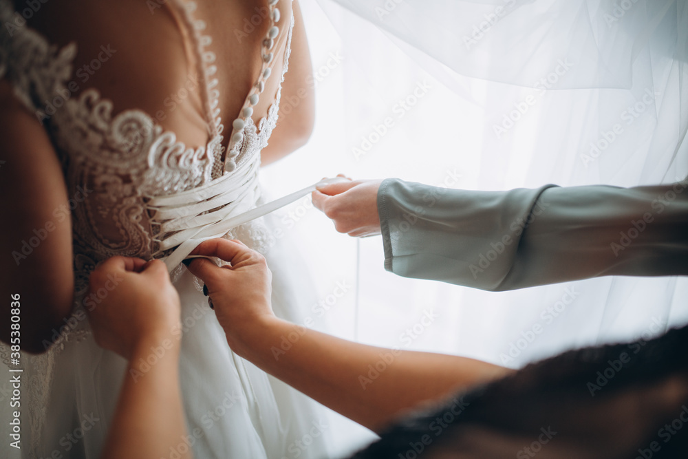 Fototapeta premium Wedding morning. Side view of bride in wedding dress. Bridesmaids preparing bride for the wedding day