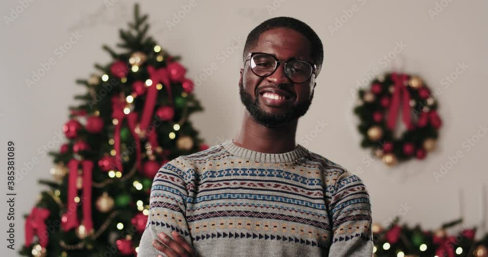 Portrait of happy african american man in glasses and winter sweater smiling at camera on background of Christmas decorations at home. Portrait of happy african american man in glasses and winter sweater smiling at camera on background of Christmas decorations at home.