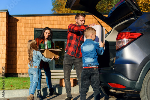 Canvas Print Joyful family helping each other to unload auto's trunk from carton boxes and su