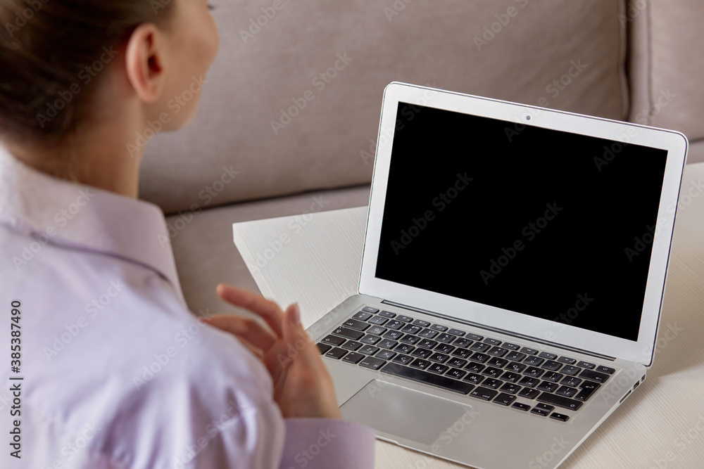 Laptop with a black blank screen, the girl is sitting back. Communicate online by video using the app.