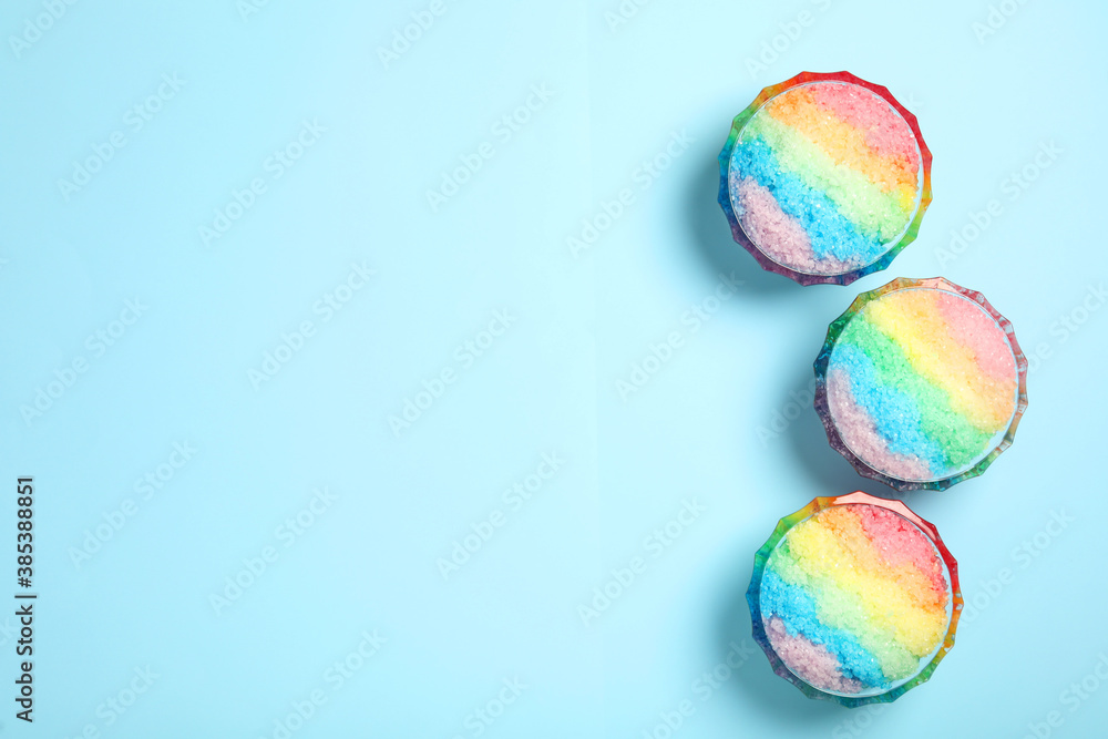Rainbow shaving ice in glass dessert bowls on light blue background, flat lay. Space for text Rainbow shaving ice in glass dessert bowls on light blue background, flat lay. Space for text