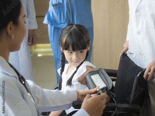 A patient, a girl in a wheelchair, is taking blood pressure measurements, followed by a female doctor among the encouraging doctors.