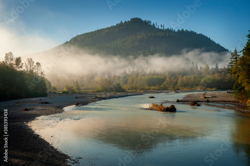 Foggy Morning Along the Nooksack River. Atmospheric view of this beautiful river as fog creeps over the tree line and the sun illuminates the trees and riverbend. photo