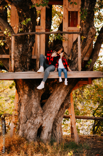 Принти на полотні Young mother in a red shirt with her daughter in a tree house