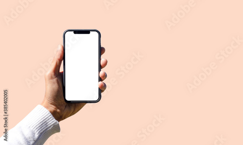 Hand holding black smartphone with white screen on soft pink background and copy space, Mobile phone frameless design concept