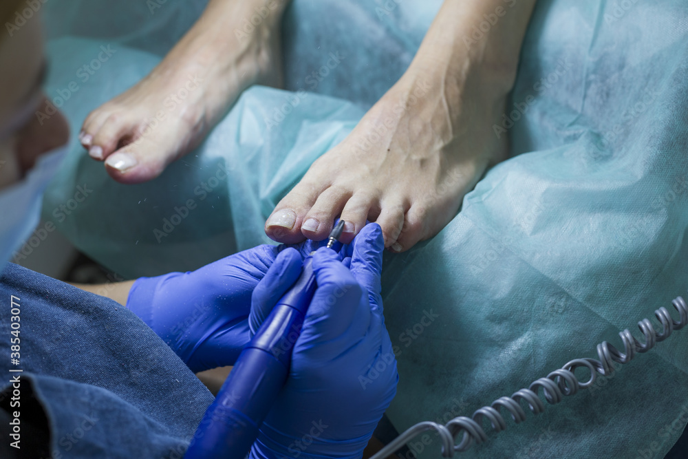Close up of doctor in gloves making procedure for foot. Pedicure in beauty spa salon. Beautician polishing nails. Foot care treatment and nail, the woman at the beautician for pedicure. 
