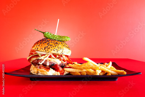 Hamburguesa con chile jalapeño acompañada de papas a la francesa con una toma frontal  en fondo rojo photo