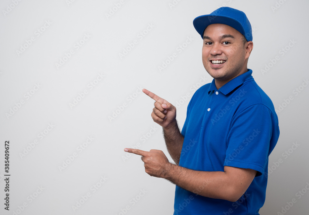 Young smiling asian delivery man in blue uniform and pointing finger on blank space isolated white background. Young smiling asian delivery man in blue uniform and pointing finger on blank space isolated white background.