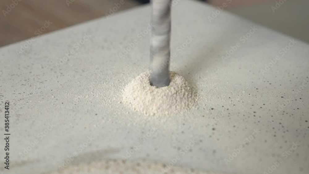 Close up of a metal drill drilling a hole in concrete and pile of shavings forming around it. Close up of a metal drill drilling a hole in concrete and pile of shavings forming around it.