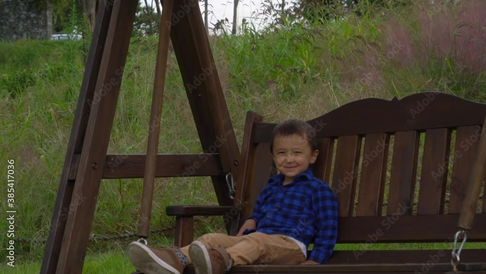 Young Boy Sitting On Swing Smiles and Waves At Camera Young Boy Sitting On Swing Smiles and Waves At Camera