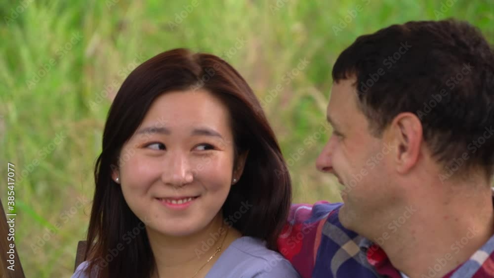 Loving International Couple Smile At Each Other As They Sit On Wooden Swing Loving International Couple Smile At Each Other As They Sit On Wooden Swing