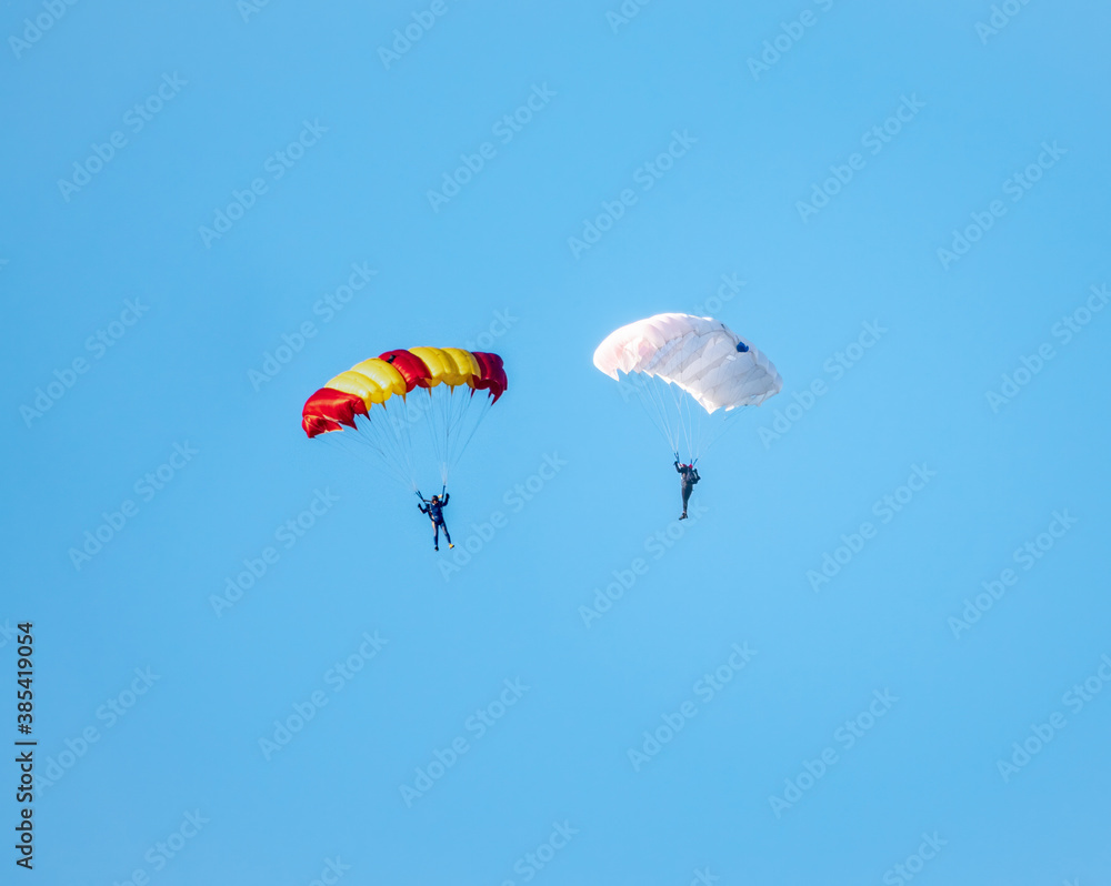 Two parachutists with white parachute floats slowly at low altitude on the background of clear sky Two parachutists with white parachute floats slowly at low altitude on the background of clear sky