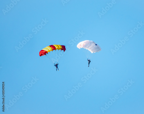 Two parachutists with white parachute floats slowly at low altitude on the background of clear sky