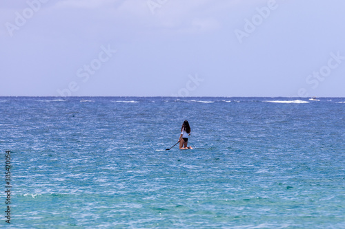 Young woman in white t-shirt and white long black hair standing on a knees on paddle board in the middle of an ocean © Dmitry