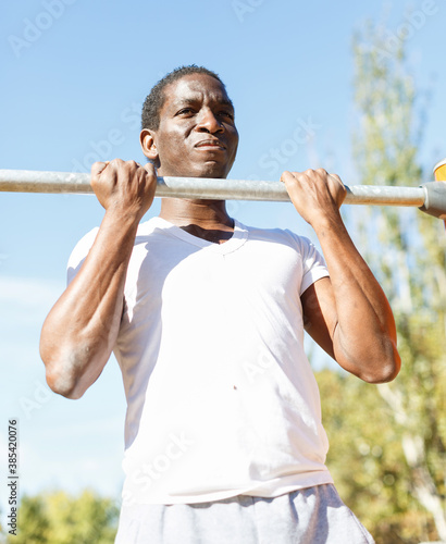 Portrait of active african american man doing workout at pull-up bar in park