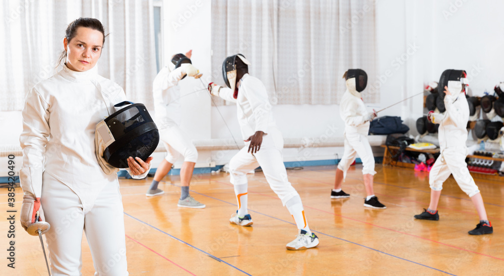 Portrait of smiling sporty young cheerful positive glad woman with foil at fencing workout