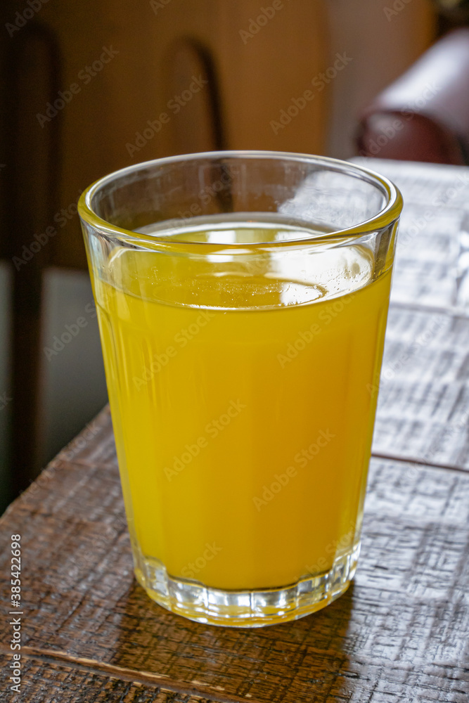A glass of fresh orange juice drink on brown table in living room. A glass of fresh orange juice drink on brown table in living room.
