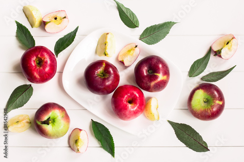 Fototapeta Naklejka Na Ścianę i Meble -  Apple slices, apples, green leaves on a white background top view. background with apples in a white plate on a white table.