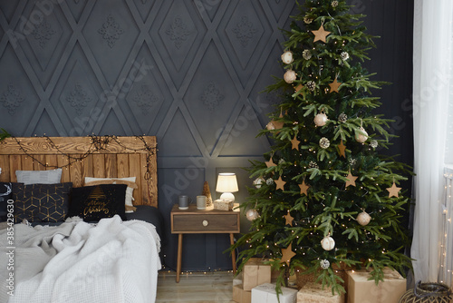 Christmas decorated bedroom interior with comfortable bed, Christmas fir tree and gift boxes on floor, copy space. Cozy home moment. Happy New Year. Christmas morning