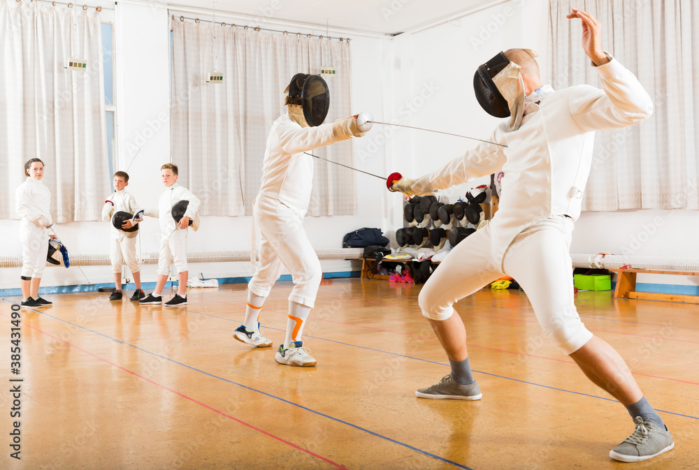 Fototapeta premium Athletic group practicing effective fencing techniques in sparring in training room