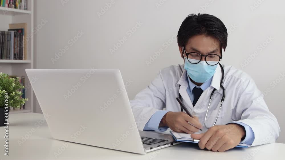 Young Asian Doctor Man in Lab Coat or Gown with Stethoscope Wear Glasses and Face Mask Writing Patient Exam Report in Office Young Asian Doctor Man in Lab Coat or Gown with Stethoscope Wear Glasses and Face Mask Writing Patient Exam Report in Office