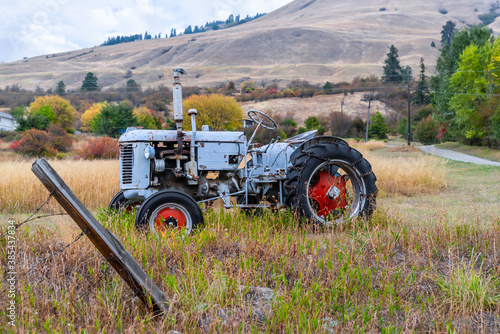 An old tractor stands in the grass against the background of colorful autumn trees and hills