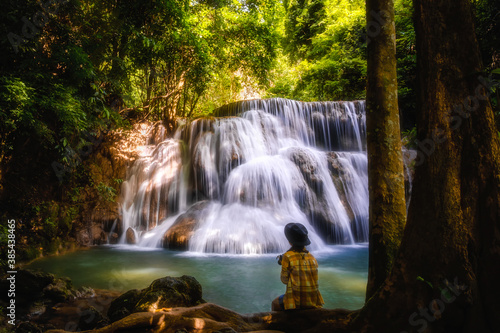 Young woman sitting on the rock and enjoying waterfall landscape. Travel concept adventure Huay Mae Khamin Waterfall Thailand