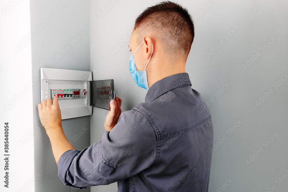 an electrician repairing a mask switch during a pandemic covid - 19. Hands of electrician with electric actuator equipment in fuse box an electrician repairing a mask switch during a pandemic covid - 19. Hands of electrician with electric actuator equipment in fuse box