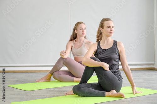 Couple of healthy young Caucasian women wearing sportswear with strength posture doing sitting Yoga workout at home.