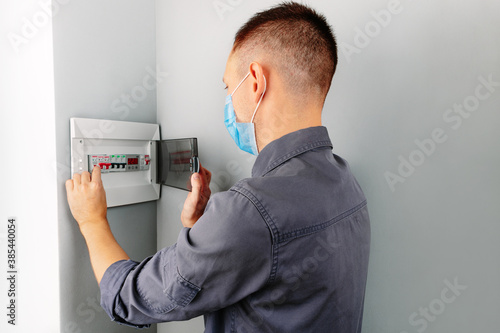 an electrician repairing a mask switch during a pandemic covid - 19. Hands of electrician with electric actuator equipment in fuse box