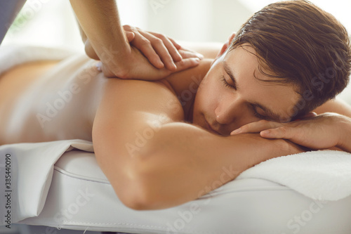 Young man lying on massage table with eyes closed enjoying professional relaxing back massage photo
