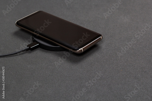 Wireless charging for phone on black background. Smartphone charges on fast induction charger.