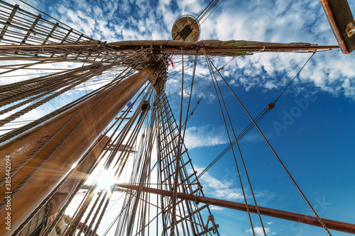 Up view of the tall ship mast with tight wires against sun beams and a cloudy bleu sky photo