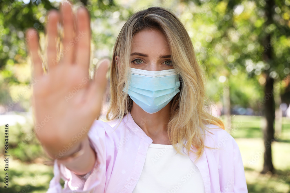 Woman in protective face mask showing stop gesture in park. Prevent spreading of coronavirus - obrazy, fototapety, plakaty 
