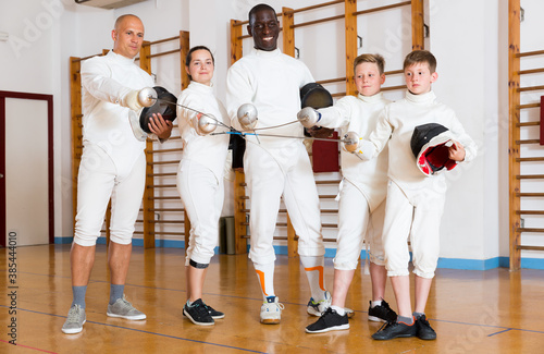 Portrait of smiling mixed age group of athletes with foils at fencing workout