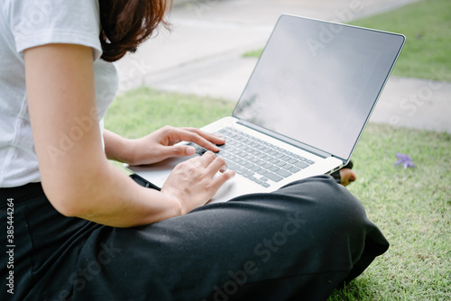 Beautiful Woman Relaxing and Using Laptop While Sitting on Grass Field, Asian Woman Working Online on Laptop Device and Joying .Social Media. Relaxation Leisure Activities Lifestyles/Work at Home