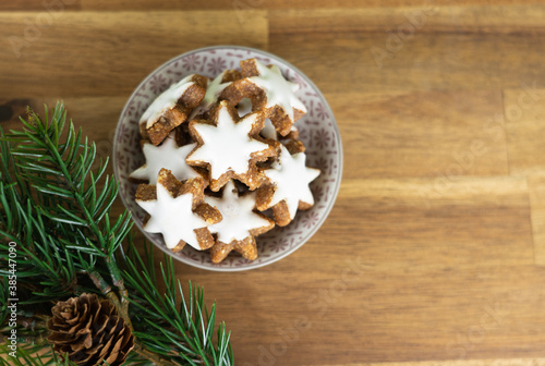 A cup with christmas biscuits on a wooden table and with fir branches, top view