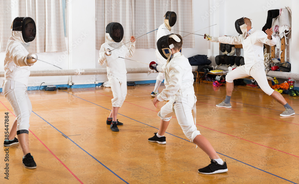 Portrait of young fencers with trainer engaged in fencing in gym