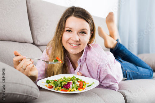 Young smiling woman enjoying tasty green salad at home © JackF