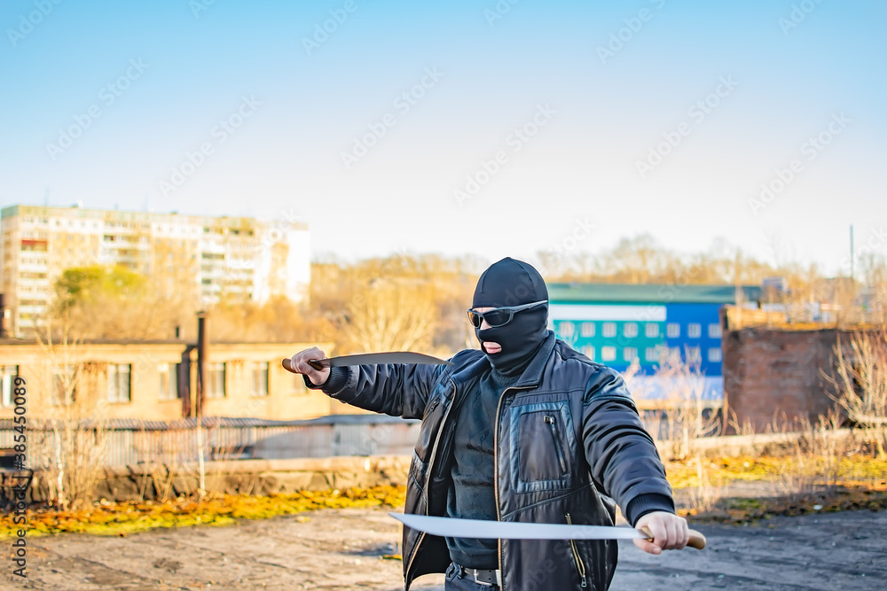 a bandit wearing black glasses and a mask trains with a machete on the ruins in an abandoned area of the city