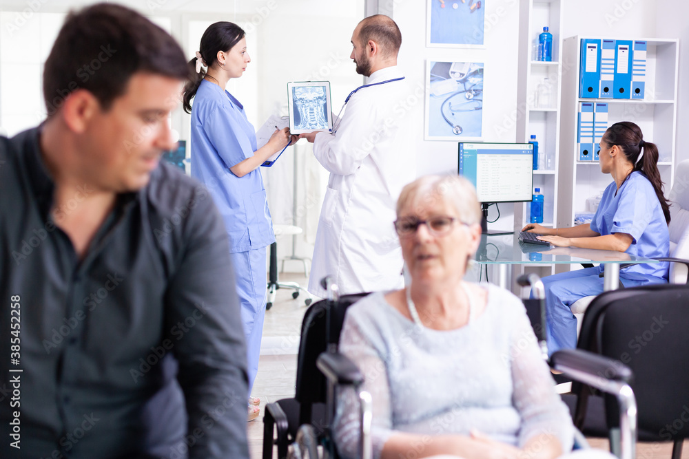 Obraz premium Doctor using tablet pc with patient x-ray while discussing with nurse in hospital hallway. Doctor wearing white coat and stethoscope. Health care system medical diagnosis disease teamwork