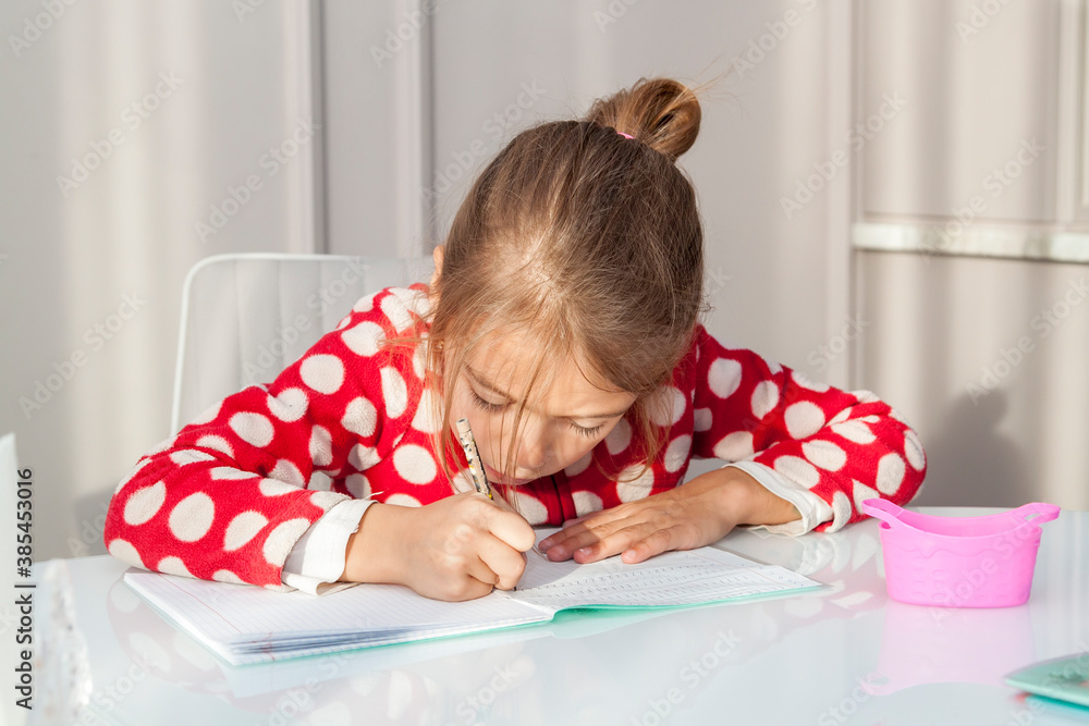 little girl doing homework sitting at kitchen table, learning at home. Hard task of reading and writing for elementary school little girl doing homework sitting at kitchen table, learning at home. Hard task of reading and writing for elementary school