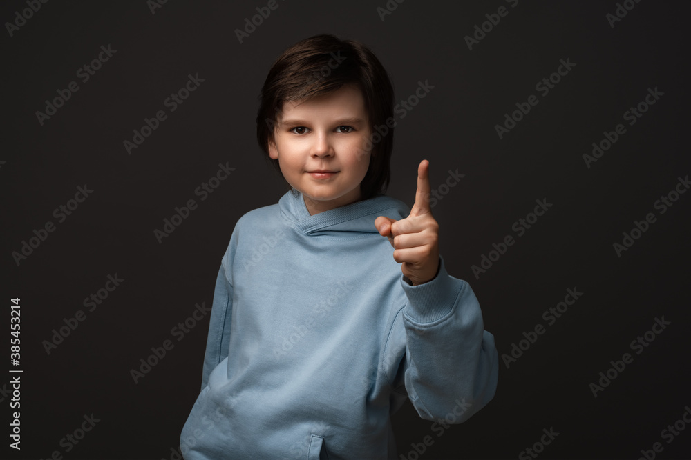 Portrait of Serious boy showing index finger. Studio shot, gray background. Human emotions, facial expression concept Portrait of Serious boy showing index finger. Studio shot, gray background. Human emotions, facial expression concept