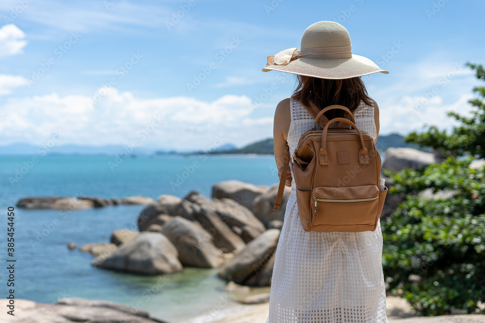 Woman traveling alone with a backpack ,standing back on the rocks, looking at the sea in front. Women travel in the sea and mountains alone.