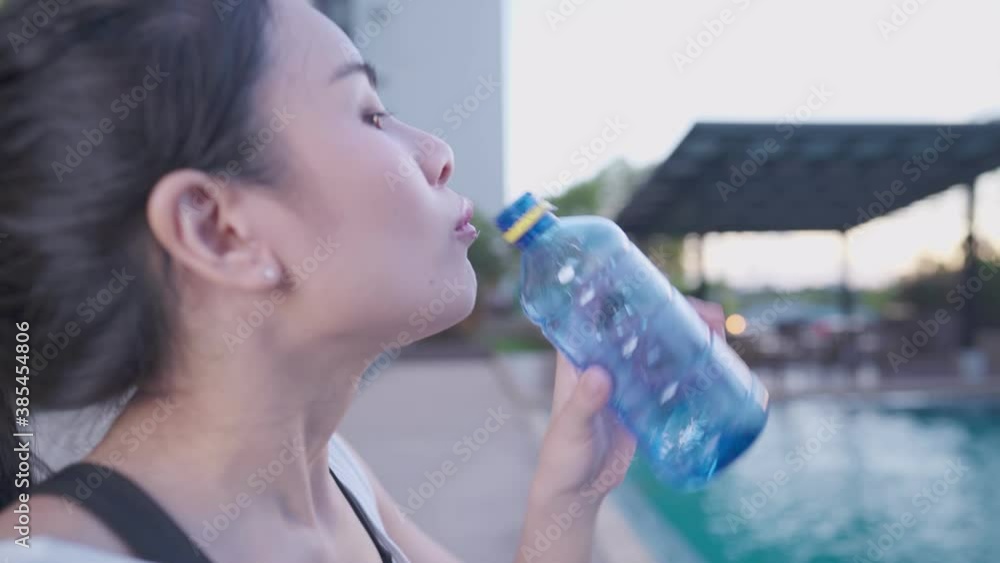 Active asian female drink water from bottle after exercising, standing by swimming pool, relaxing afternoon exercise taking a break, mineral water, stay hydrated healthy lifestyle wellness, side view Active asian female drink water from bottle after exercising, standing by swimming pool, relaxing afternoon exercise taking a break, mineral water, stay hydrated healthy lifestyle wellness, side view